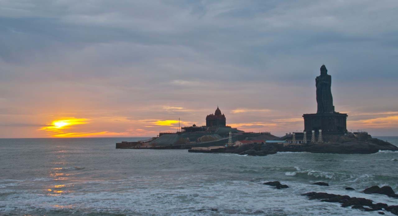Sunrise over the sea at Kanyakumari, with the Vivekananda Rock Memorial and the Thiruvalluvar statue in silhouette.
