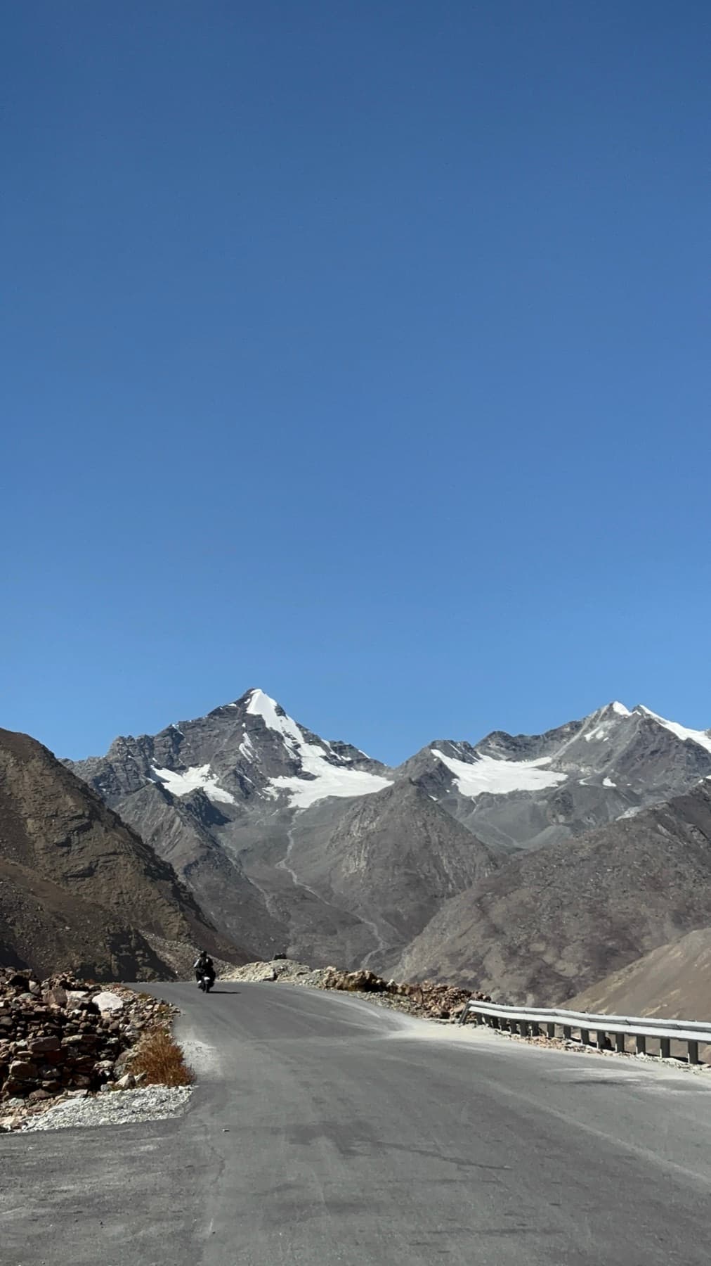 A motorcyclist climbing a high mountain road toward snow-capped peaks.