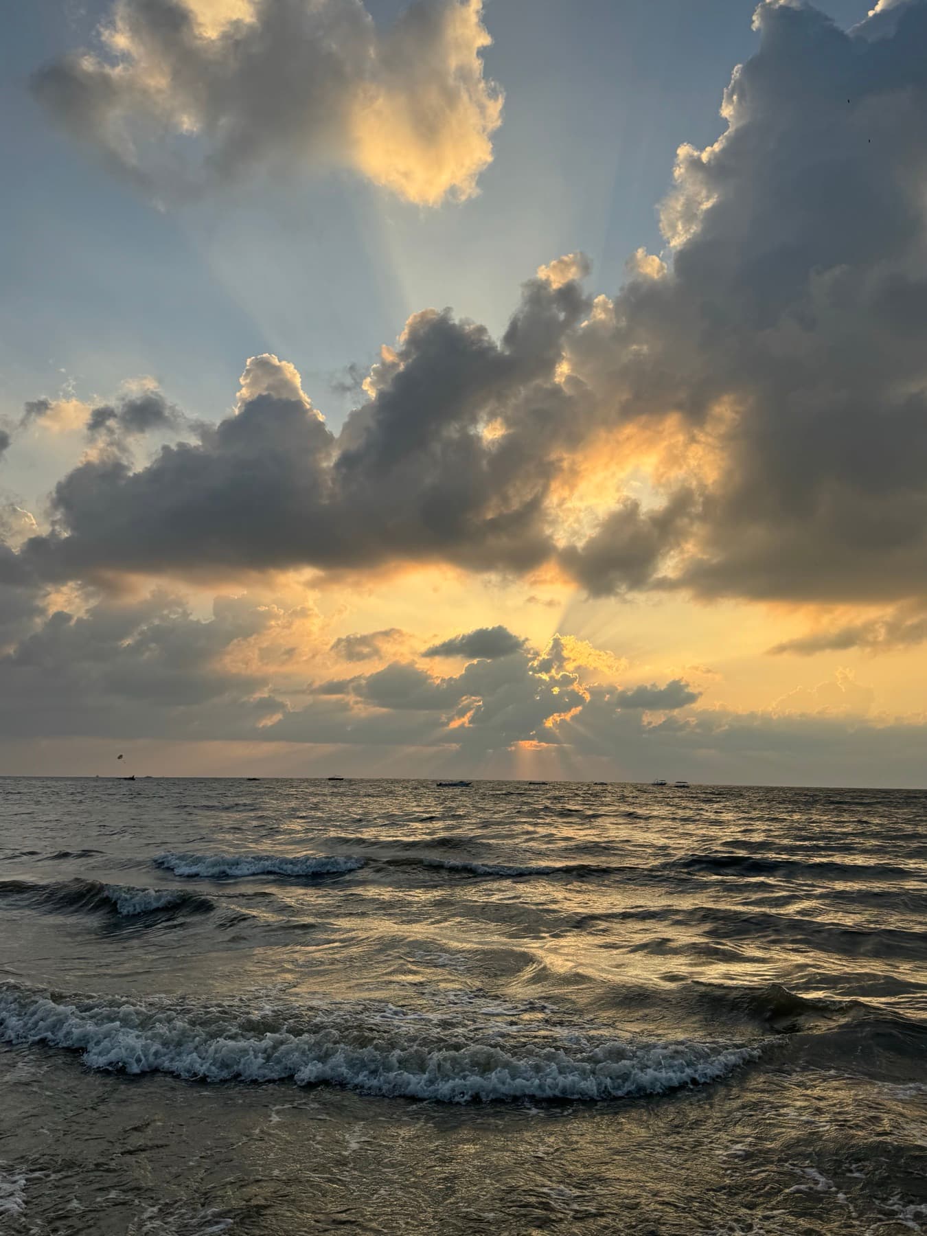 Sunlight breaking through clouds over a darkening sea, boats strung along the horizon.