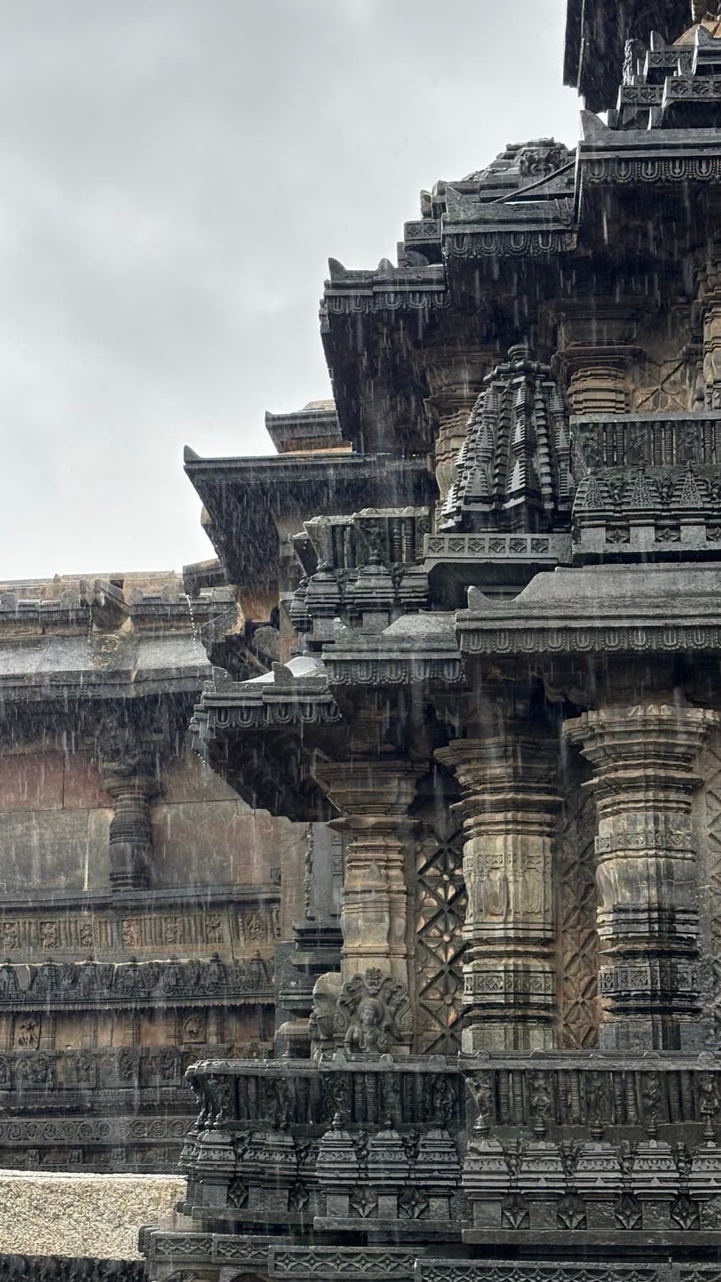 Carved stone pillars and tiered eaves of an old temple in heavy rain.