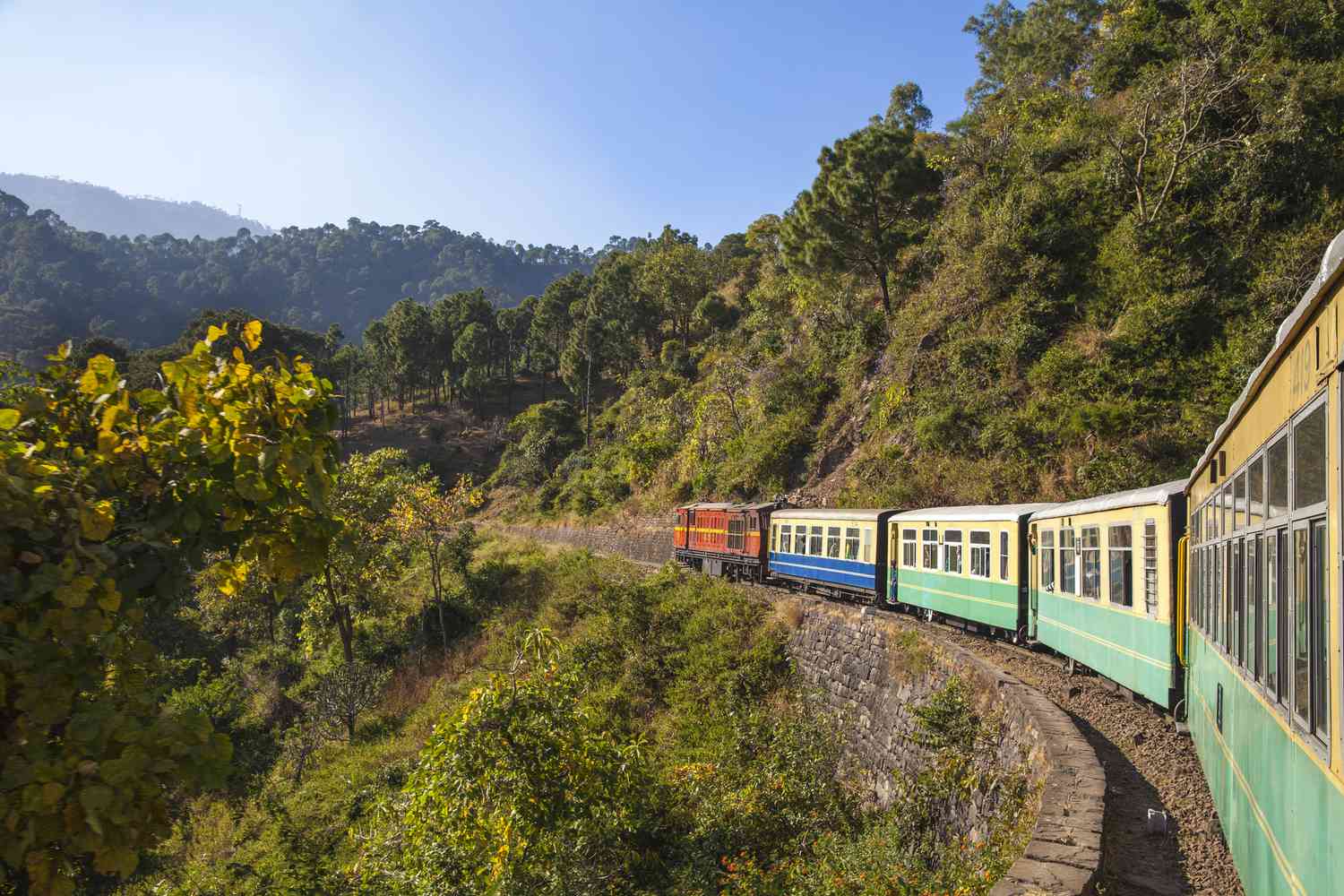 A narrow-gauge toy train curving along a forested hillside track.