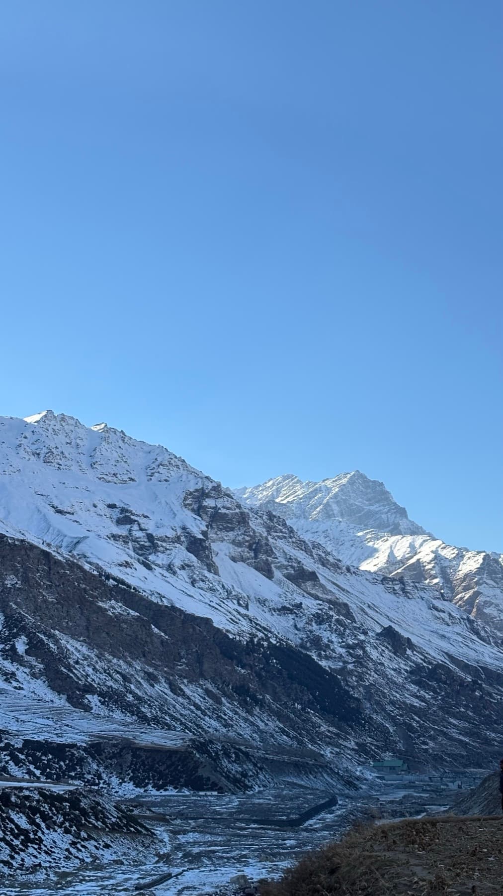 A snowbound Himalayan valley under a clear sky, a village at the foot of the mountains.